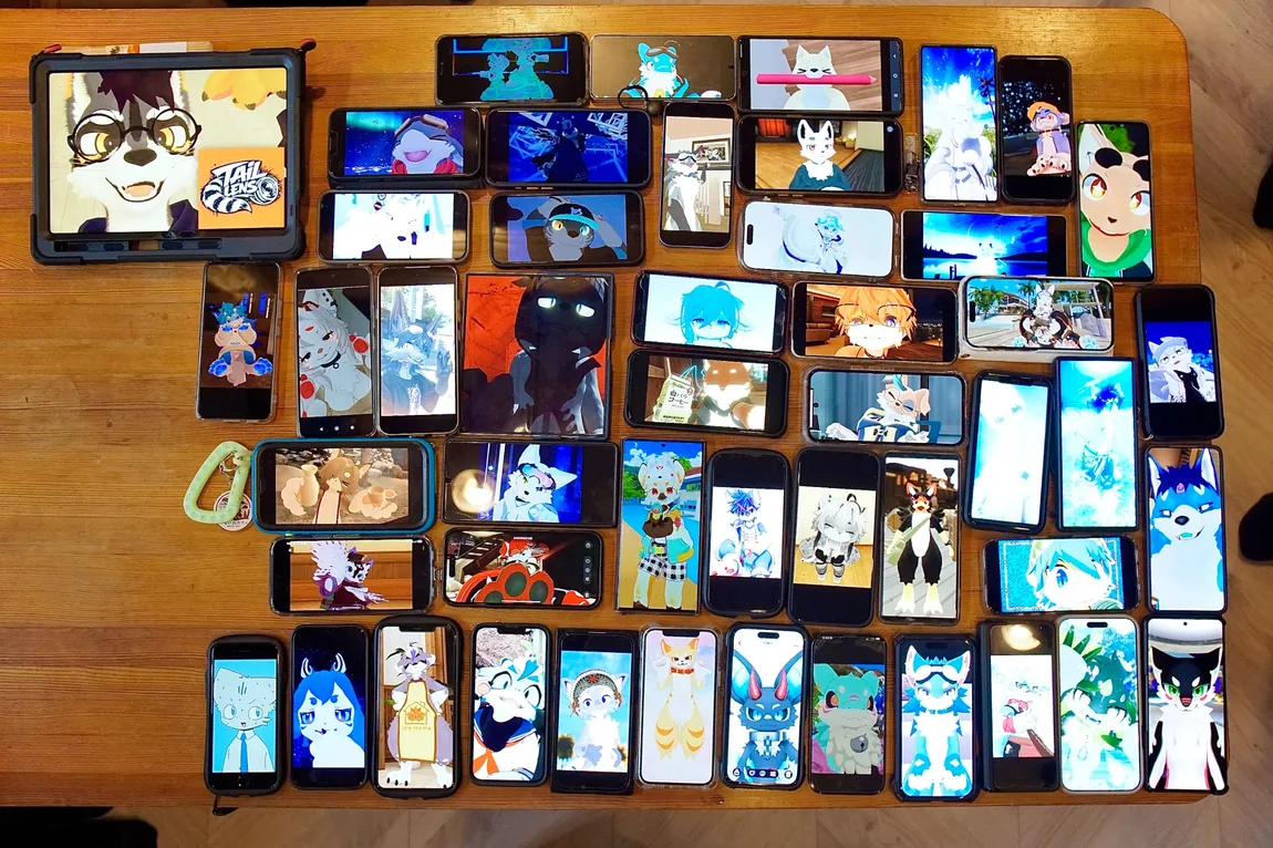 木のテーブルいっぱいに並んだスマートフォンやタブレットに動物キャラクターの画像が映っている